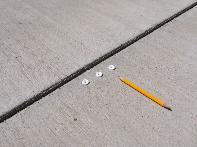 Small flush foam injection ports in a straight row in a Tempe concrete driveway